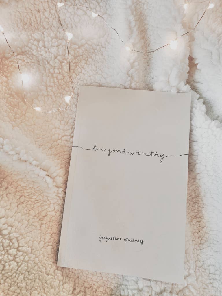 Notebook titled 'beyond worthy' by Jacqueline Whitley on a textured surface with string lights.