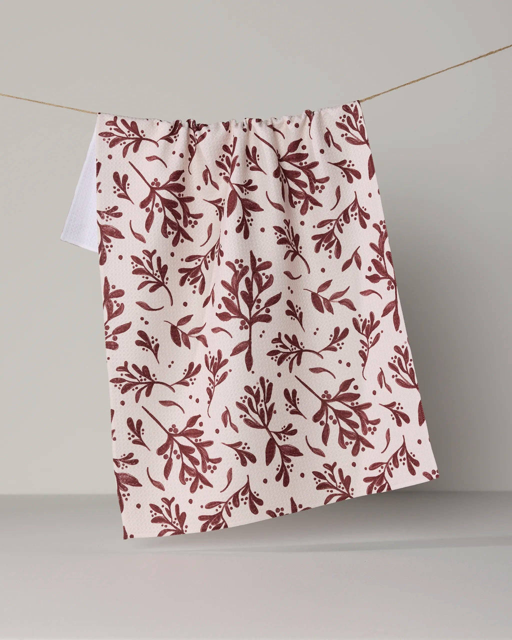 A cream-colored curtain panel with a dark red botanical leaf pattern, hanging from a thin wire against a neutral gray background.