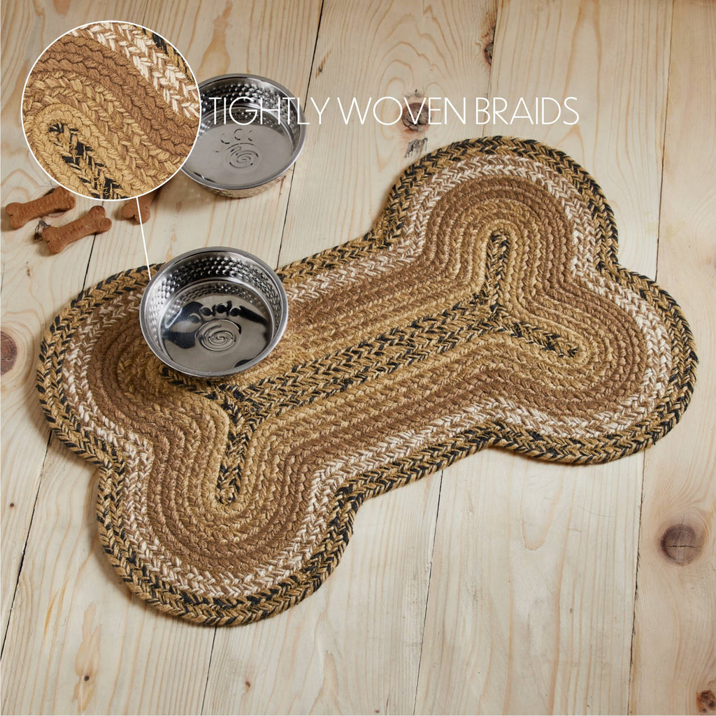A braided pet bed mat in a bone shape, shown on a light wood plank floor with two metal bowls and a circular inset showing the tightly woven braids detail.