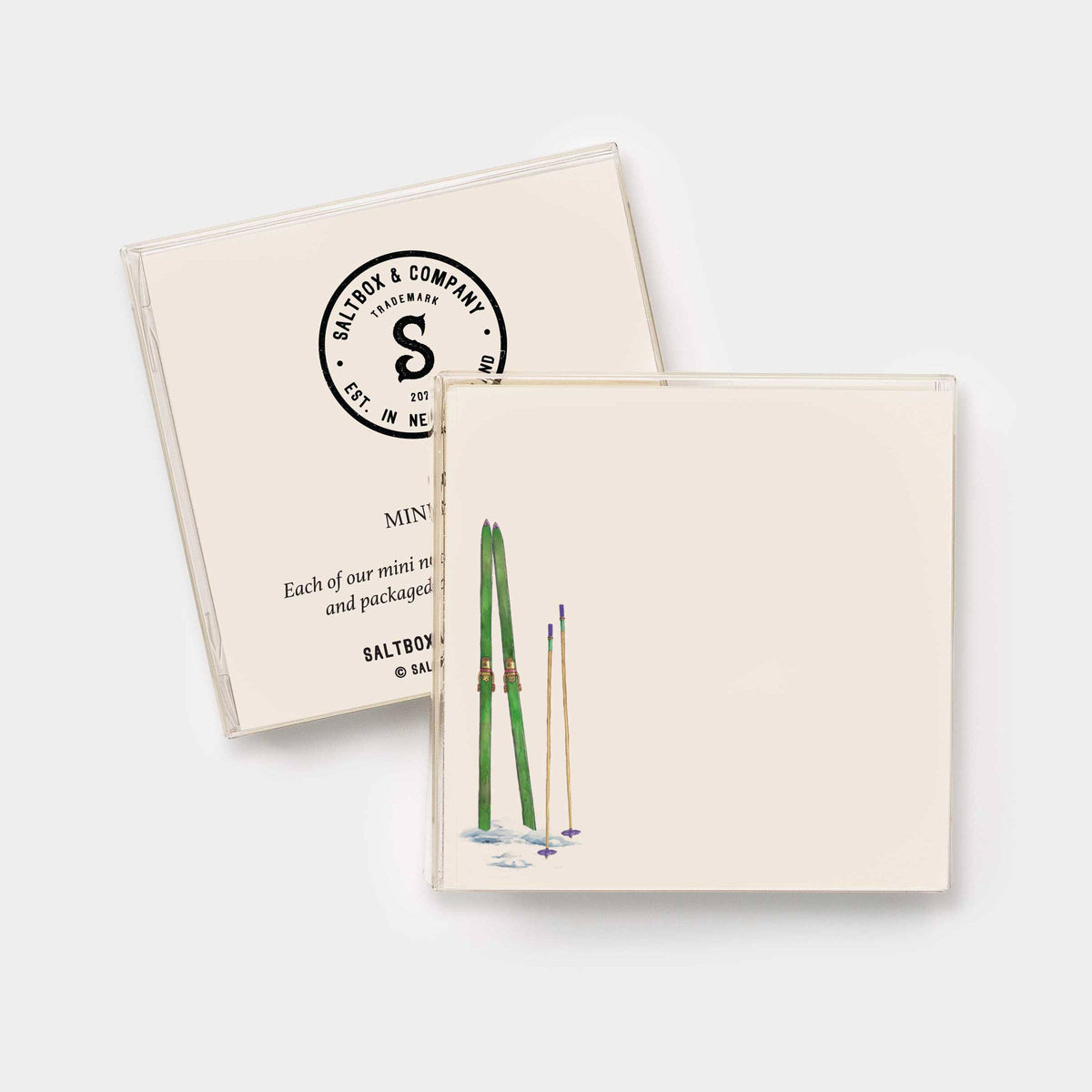 Two cream-colored square coasters with rounded corners, one featuring a black circular 'Saltbox & Company' logo and the other a watercolor illustration of green skis and ski poles, shown on a light gray background.