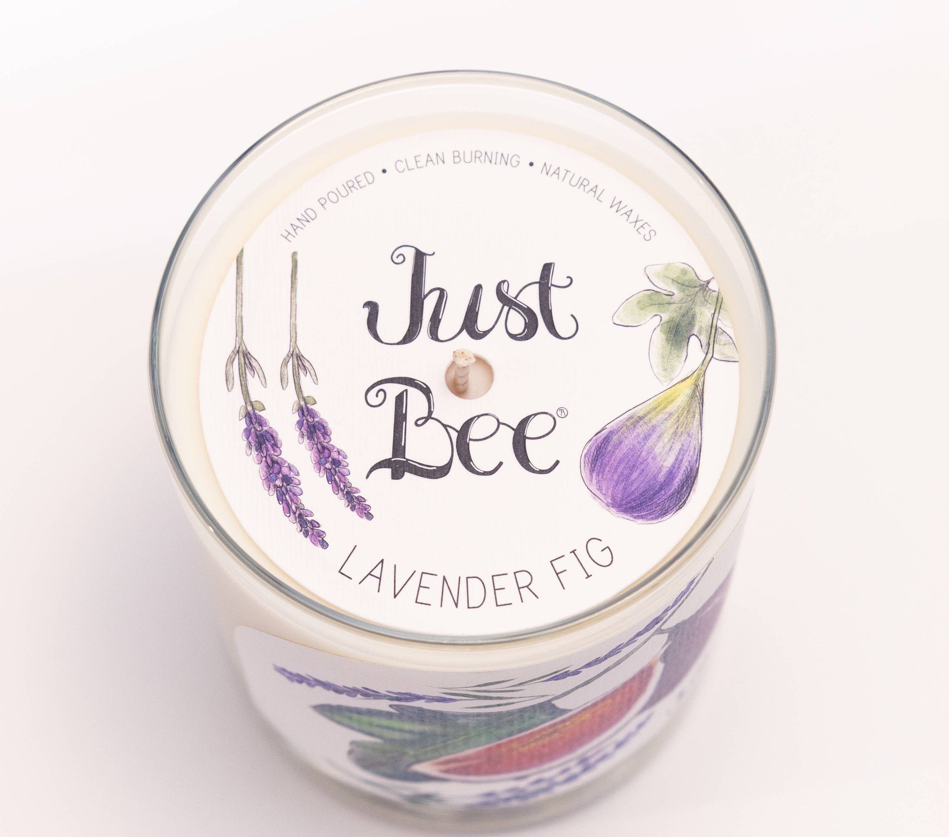 Top-down view of a glass jar candle labeled 'Just Bee' in the scent 'Lavender Fig', featuring lavender and fig illustrations on a white lid against a clean white background.
