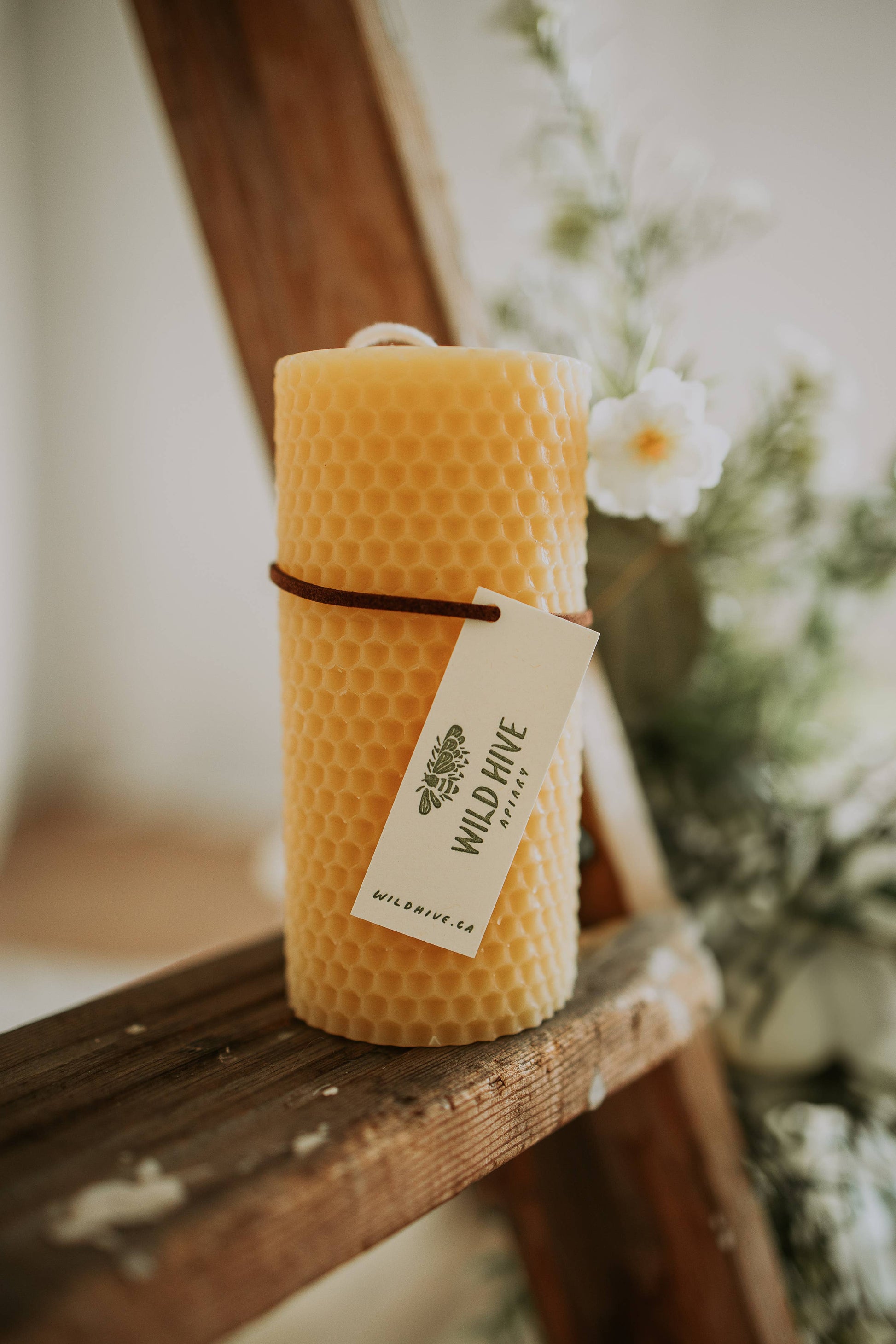 Yellow candle with a visible brand tag on a wooden surface with a blurred natural background