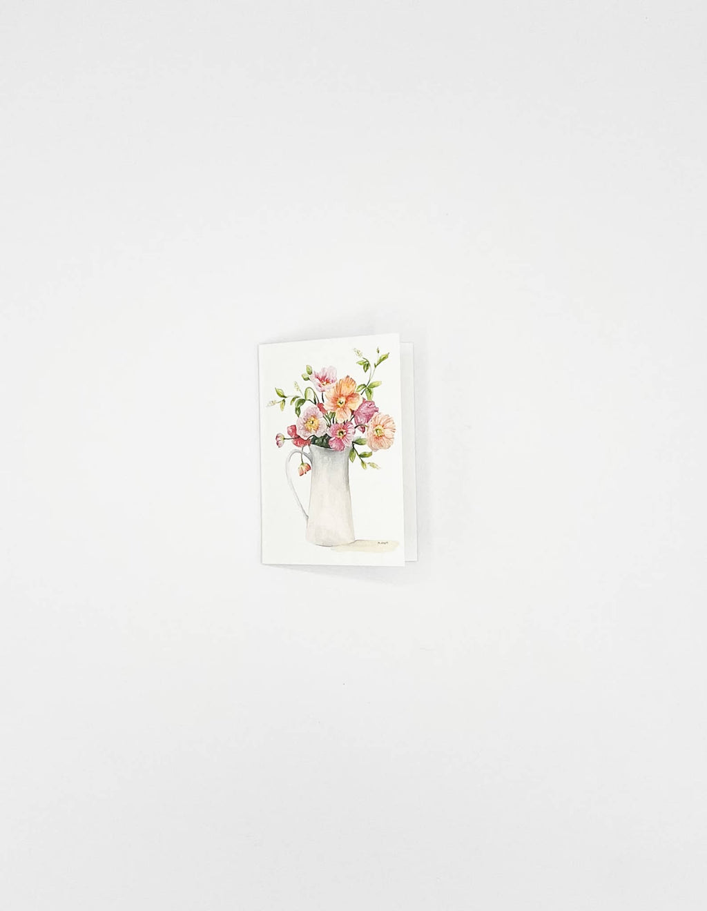 A small vertical art print or card featuring a watercolor-style bouquet of pink, peach, and yellow flowers in a white pitcher, shown against a plain white wall.