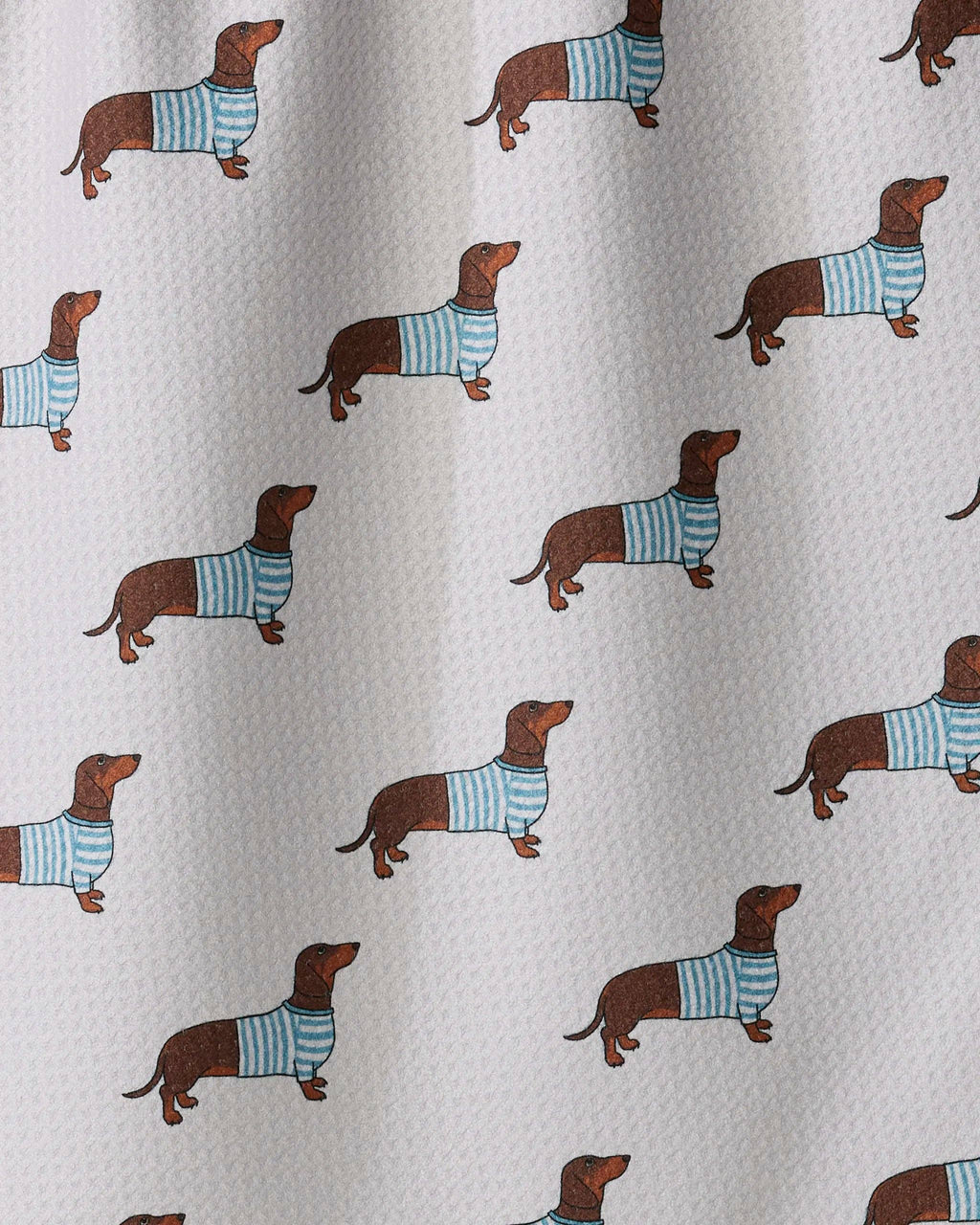 A close-up of a white textured fabric printed with a repeating pattern of brown dachshund dogs wearing light blue and white striped sweaters.