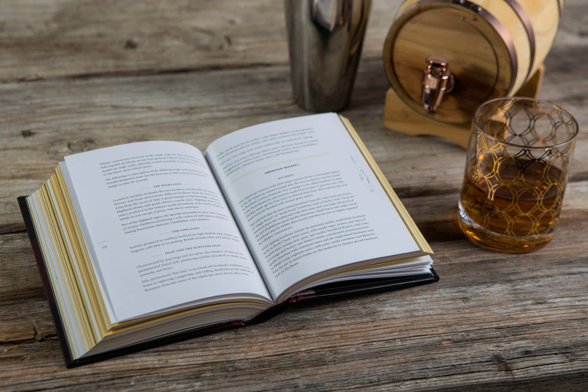 Open book on a wooden table with a glass of whiskey and a barrel in the background
