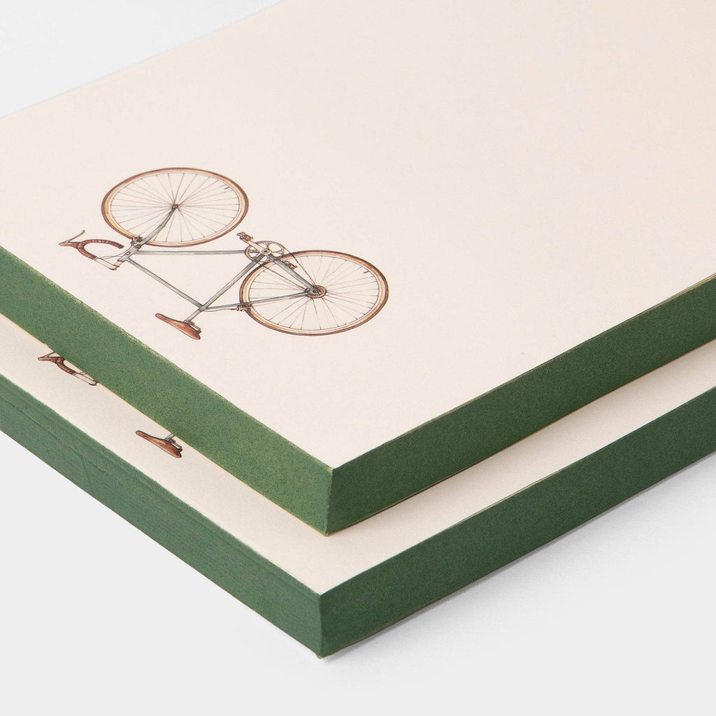 Two green notebooks with bicycle illustrations on beige backgrounds