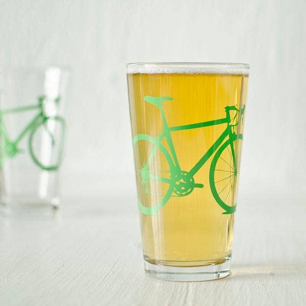 Pint glass with green bicycle design filled with beer on a white background