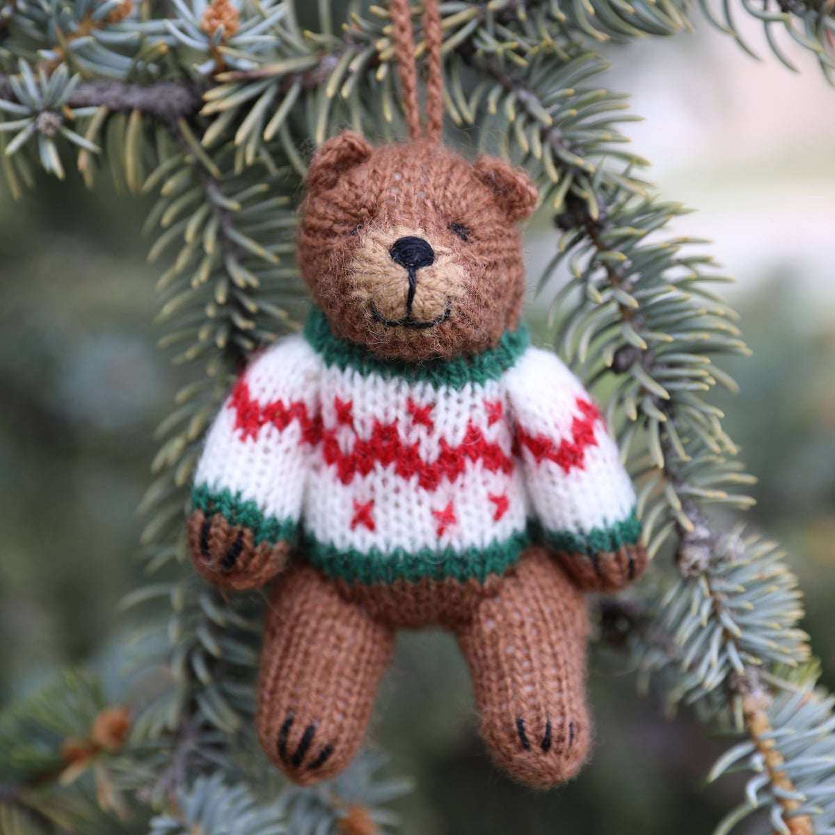 Knitted teddy bear ornament with a sweater hanging on a tree branch.