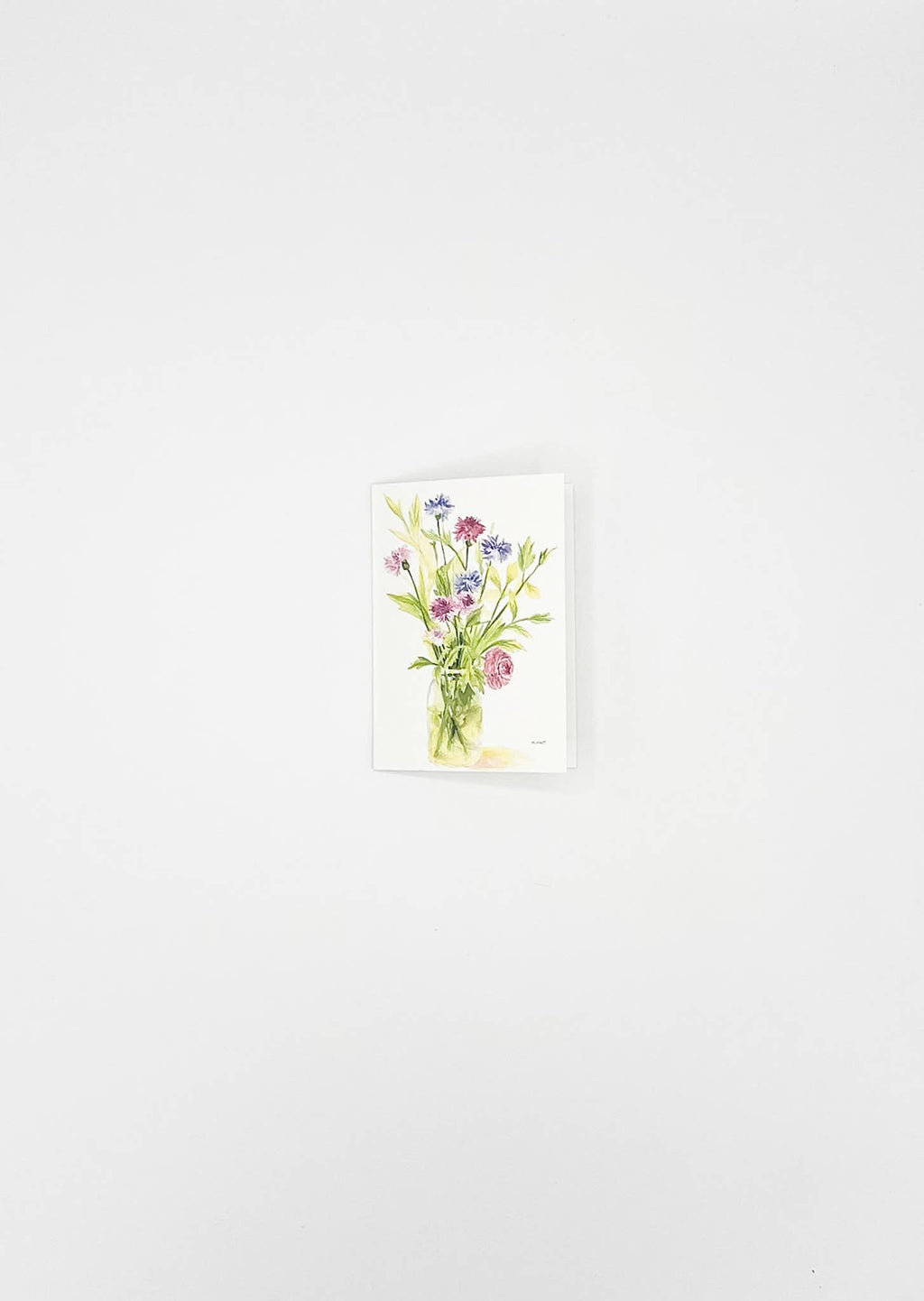 A small vertical watercolor painting of a wildflower bouquet in a clear glass vase, displayed against a plain white wall.