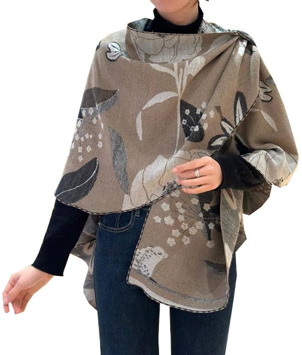 Person wearing a floral patterned poncho over a black shirt and jeans on a white background
