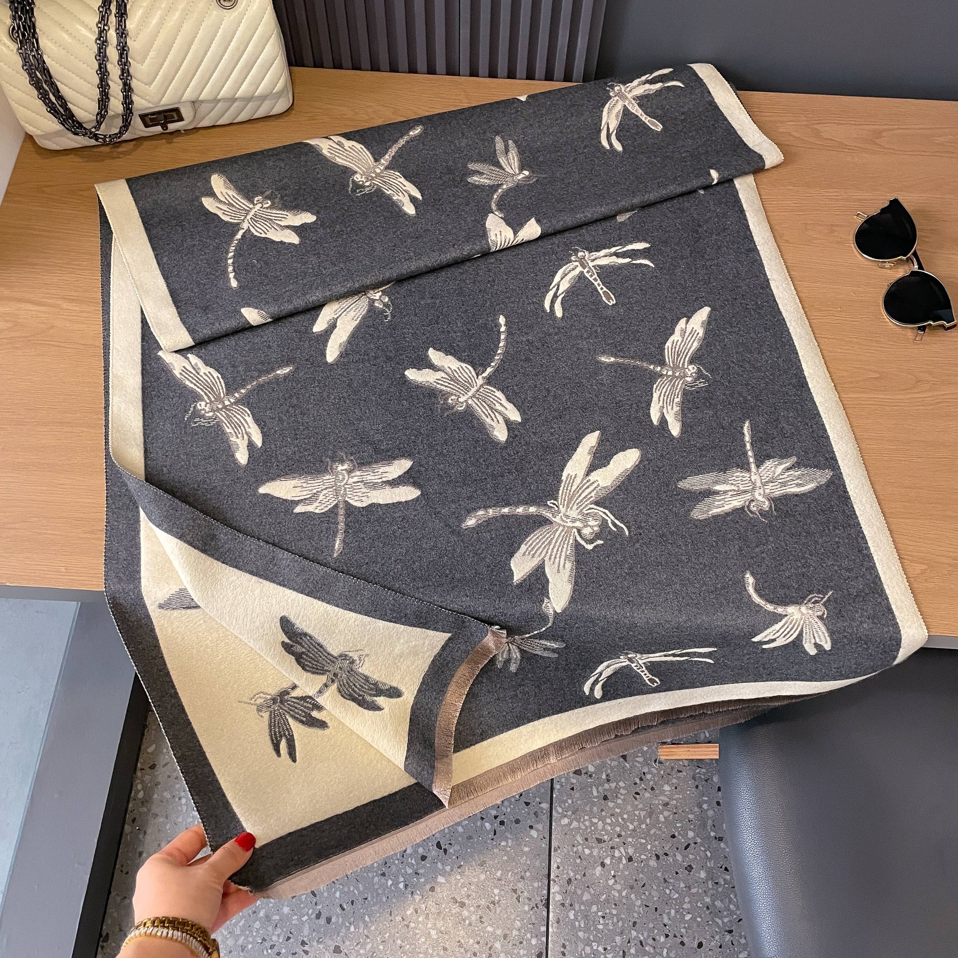 Dark gray towel with white dragonfly pattern held by a hand on a wooden surface.