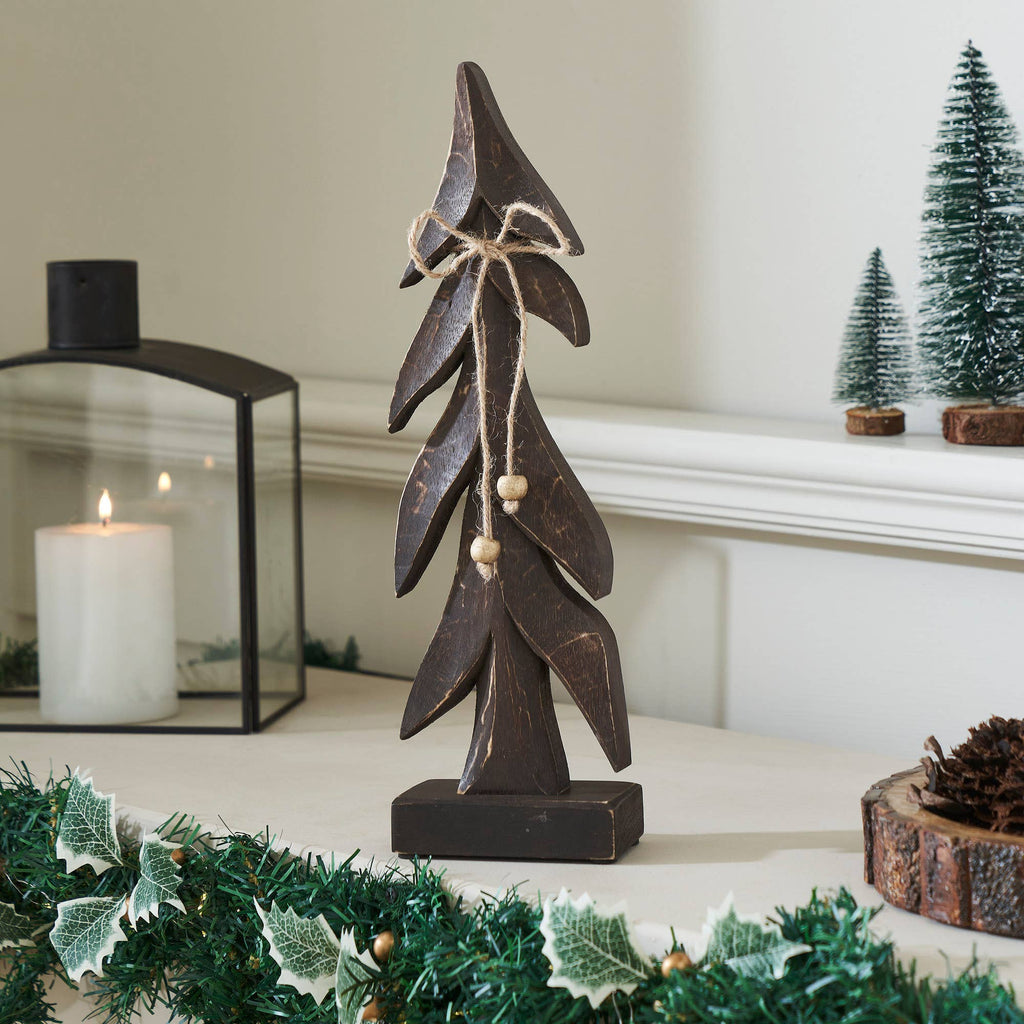 Decorative wooden tree on a mantelpiece with candles and greenery