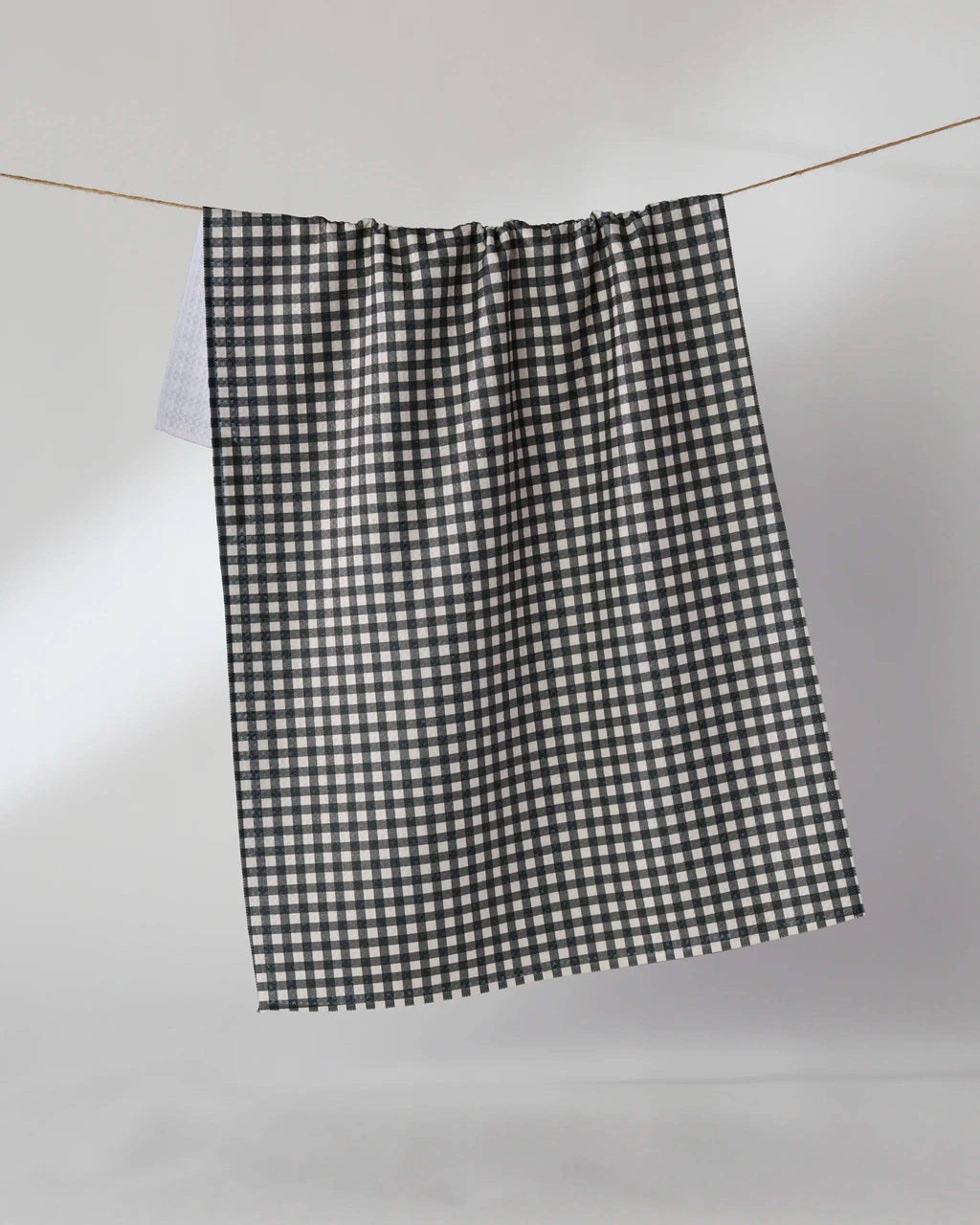 A black and white gingham checkered curtain panel hanging from a thin wire rod against a plain light gray wall.