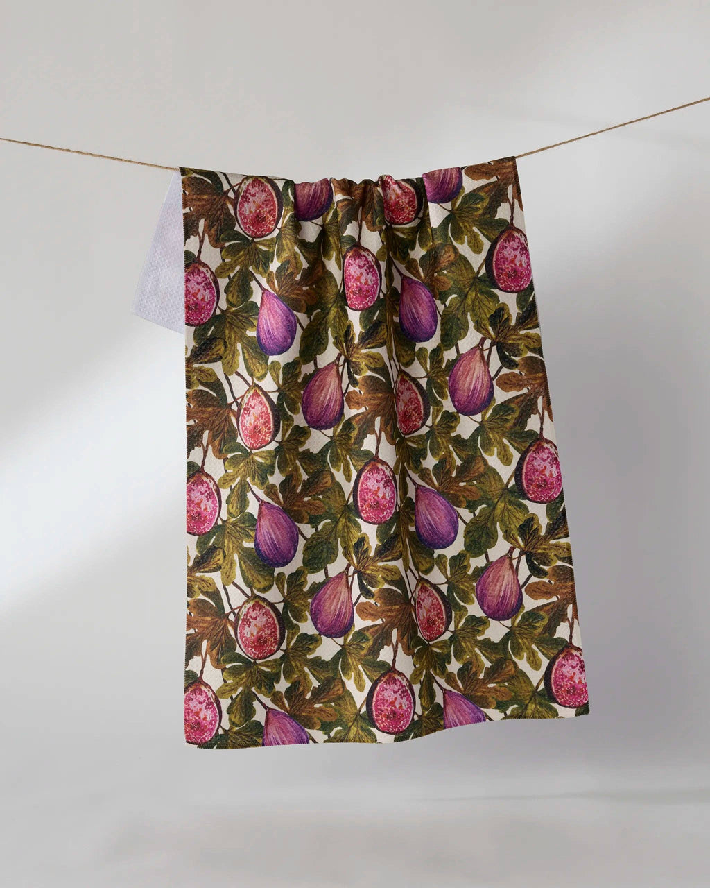 A fabric panel or curtain featuring a detailed botanical print of purple figs and green leaves on a cream background, hanging from a thin string against a plain light gray wall.
