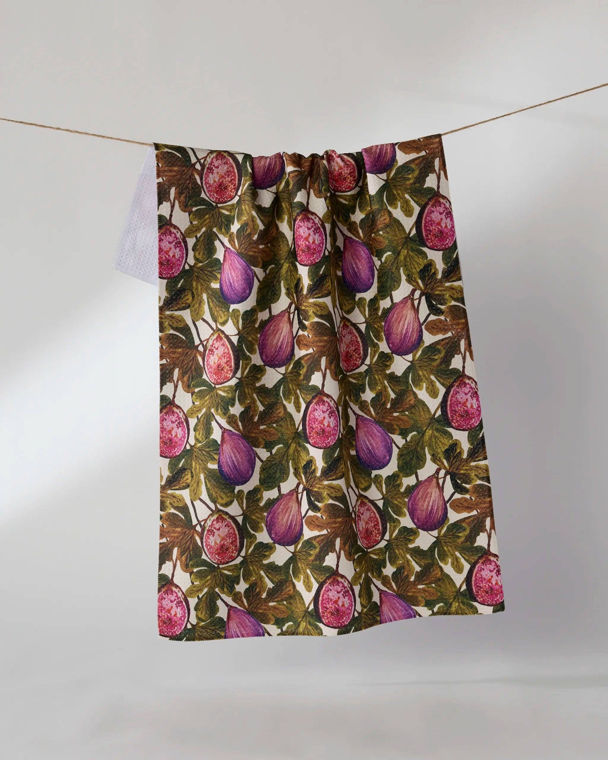 A fabric panel or curtain featuring a detailed botanical print of purple figs and green leaves on a cream background, hanging from a thin string against a plain light gray wall.