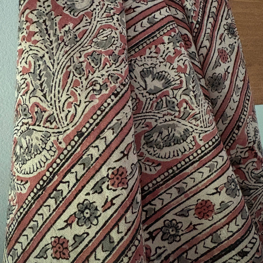 A close-up of a patterned textile with a traditional floral and geometric design in muted red, beige, gray, and black.