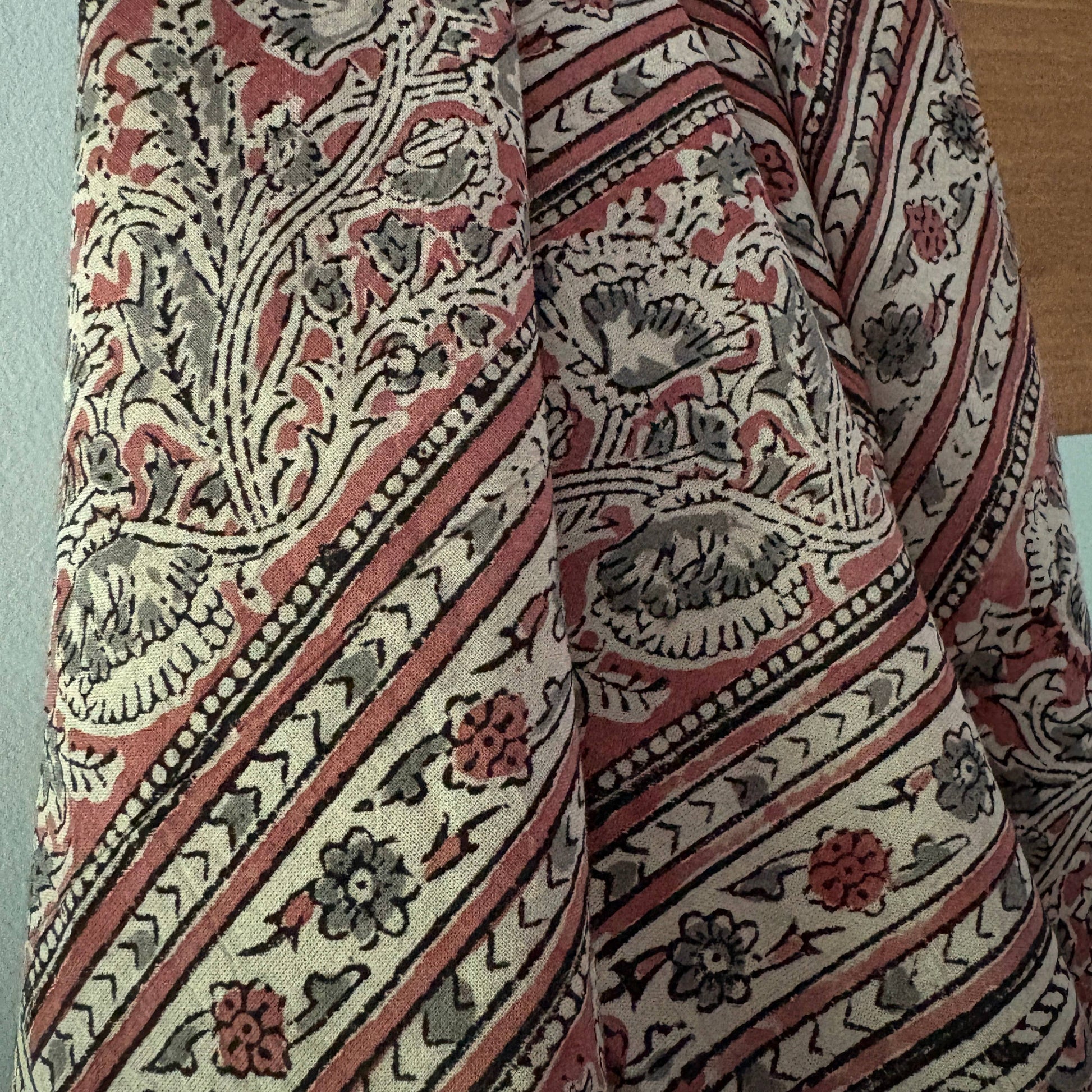 A close-up of a patterned textile with a traditional floral and geometric design in muted red, beige, gray, and black.