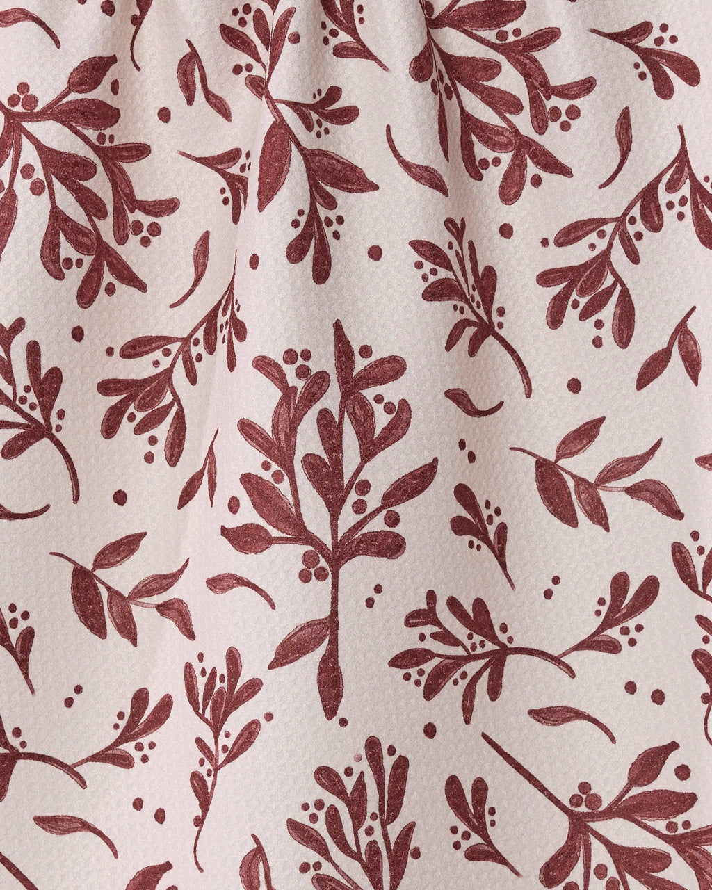 A close-up of a fabric or wallpaper pattern featuring a dusty rose-brown botanical print of mistletoe and leaves on a warm off-white background.