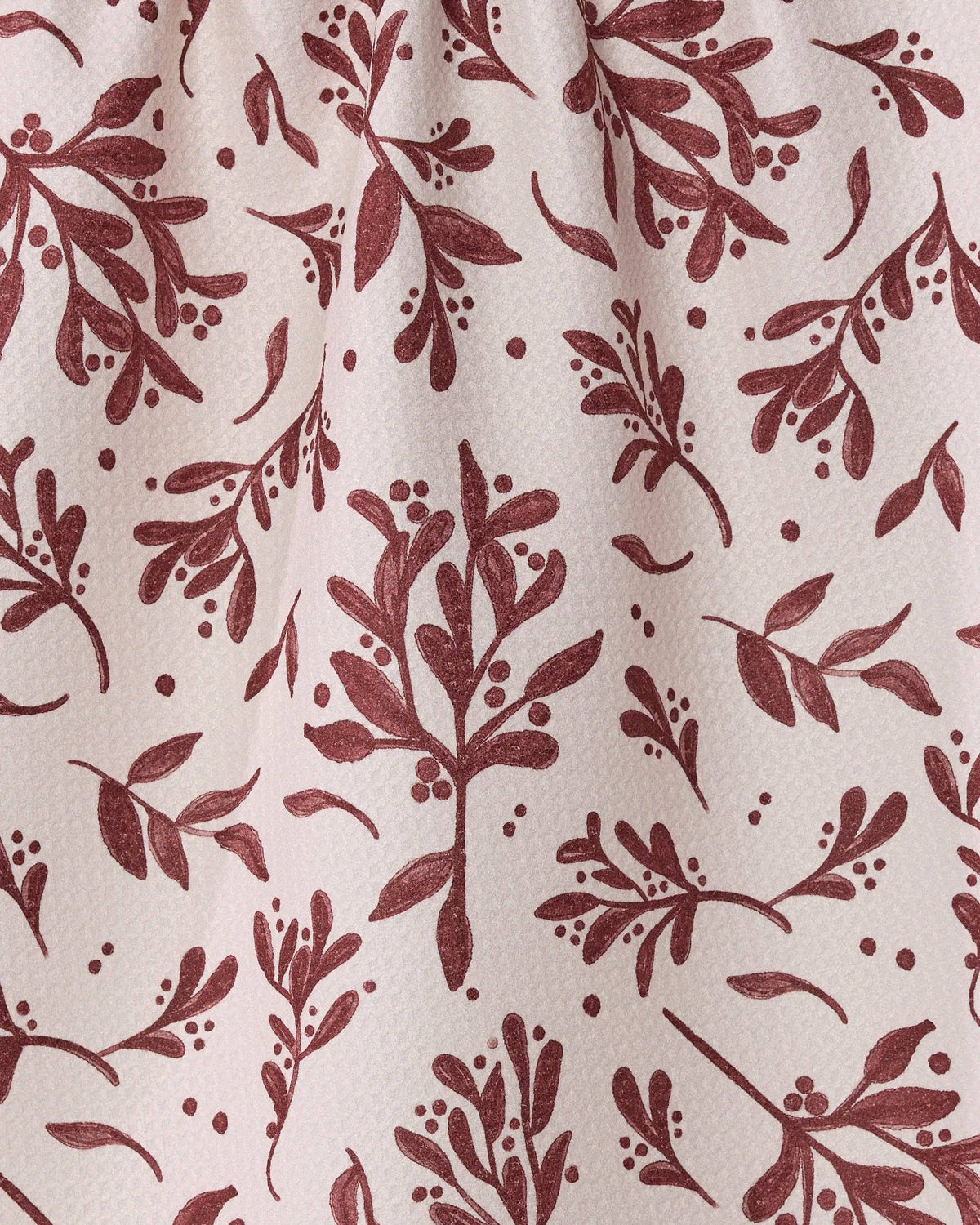 A close-up of a fabric or wallpaper pattern featuring a dusty rose-brown botanical print of mistletoe and leaves on a warm off-white background.