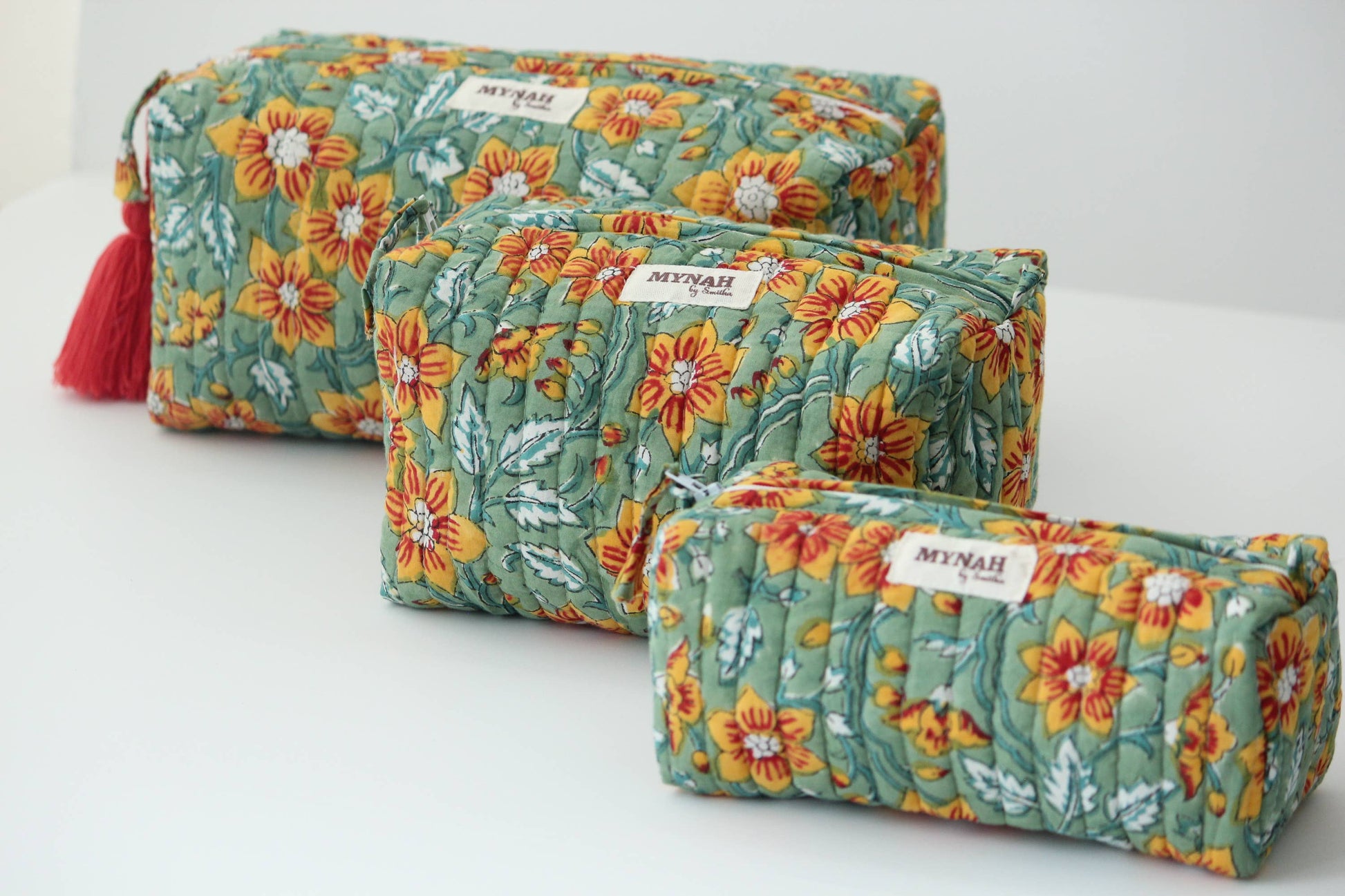 Set of three floral-patterned pouches with tassels on a white background