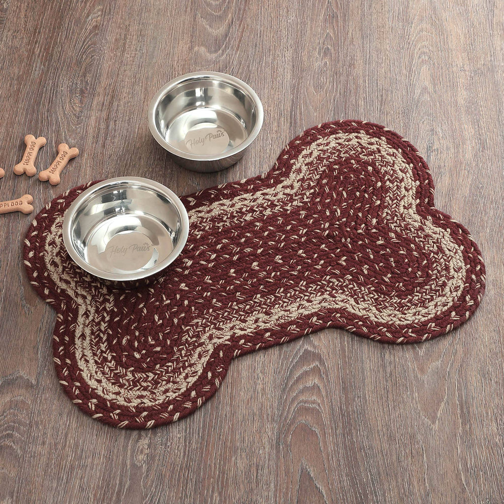 Two metal dog bowls on a braided dog bone mat on a wooden floor.