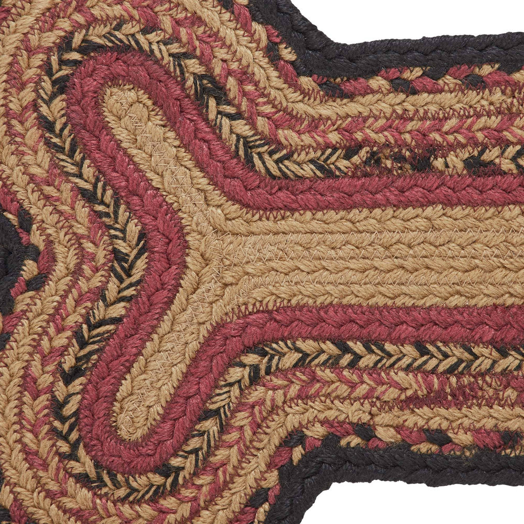 A close-up of a braided jute rug with a geometric pattern in natural tan, dusty rose, and black.