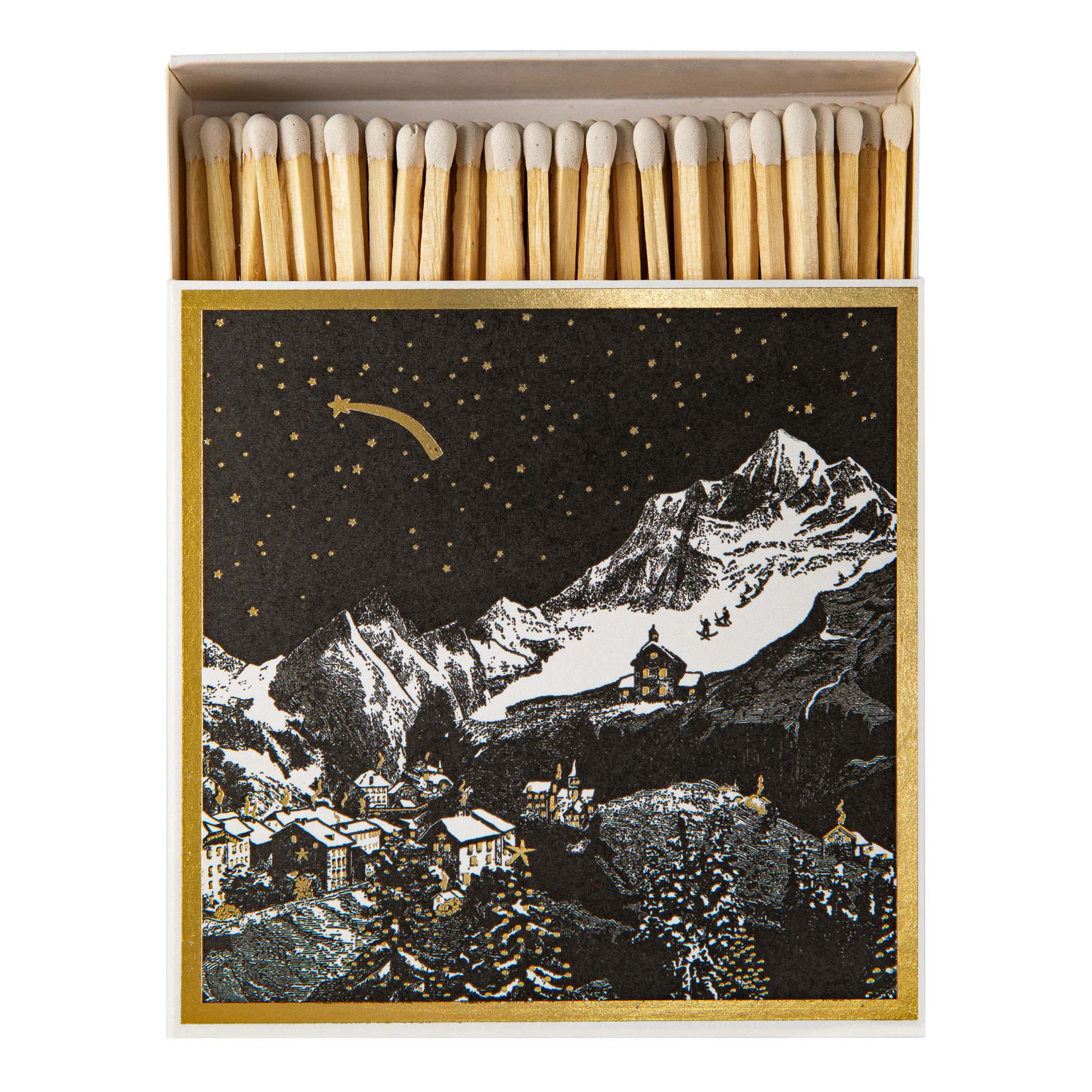 An open matchbox with natural wood matches inside and a decorative front insert showing a snowy mountain village under a starry night sky with a shooting star. The box is framed in gold and photographed on a white background.