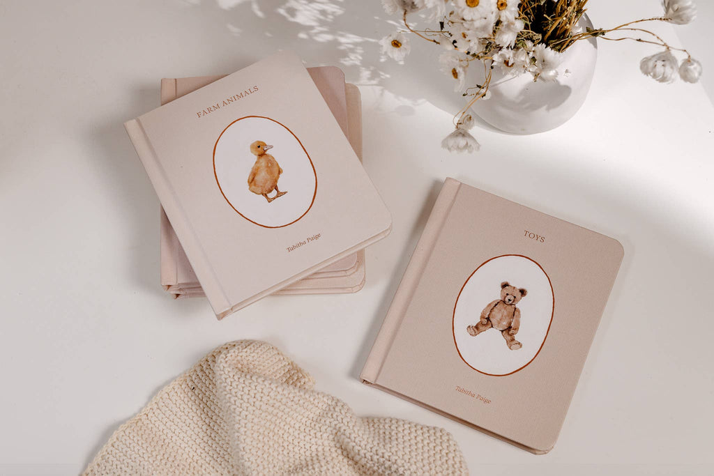 Two beige books with bear illustrations on a light surface with a vase of flowers.