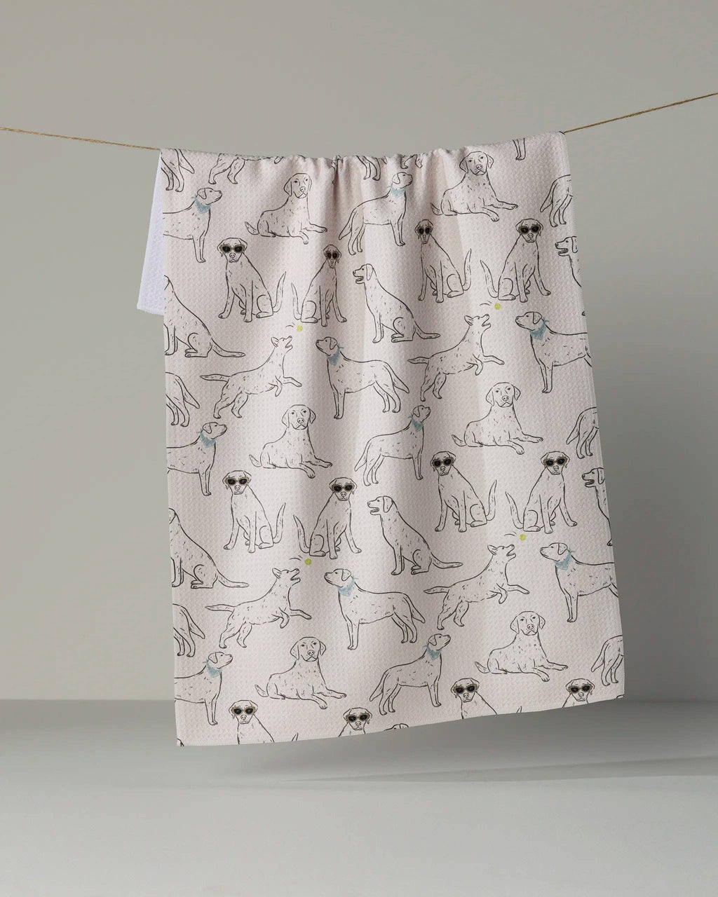 A fabric curtain panel with a repeating pattern of illustrated dogs in black and blue, hanging from a thin string against a plain light gray wall.