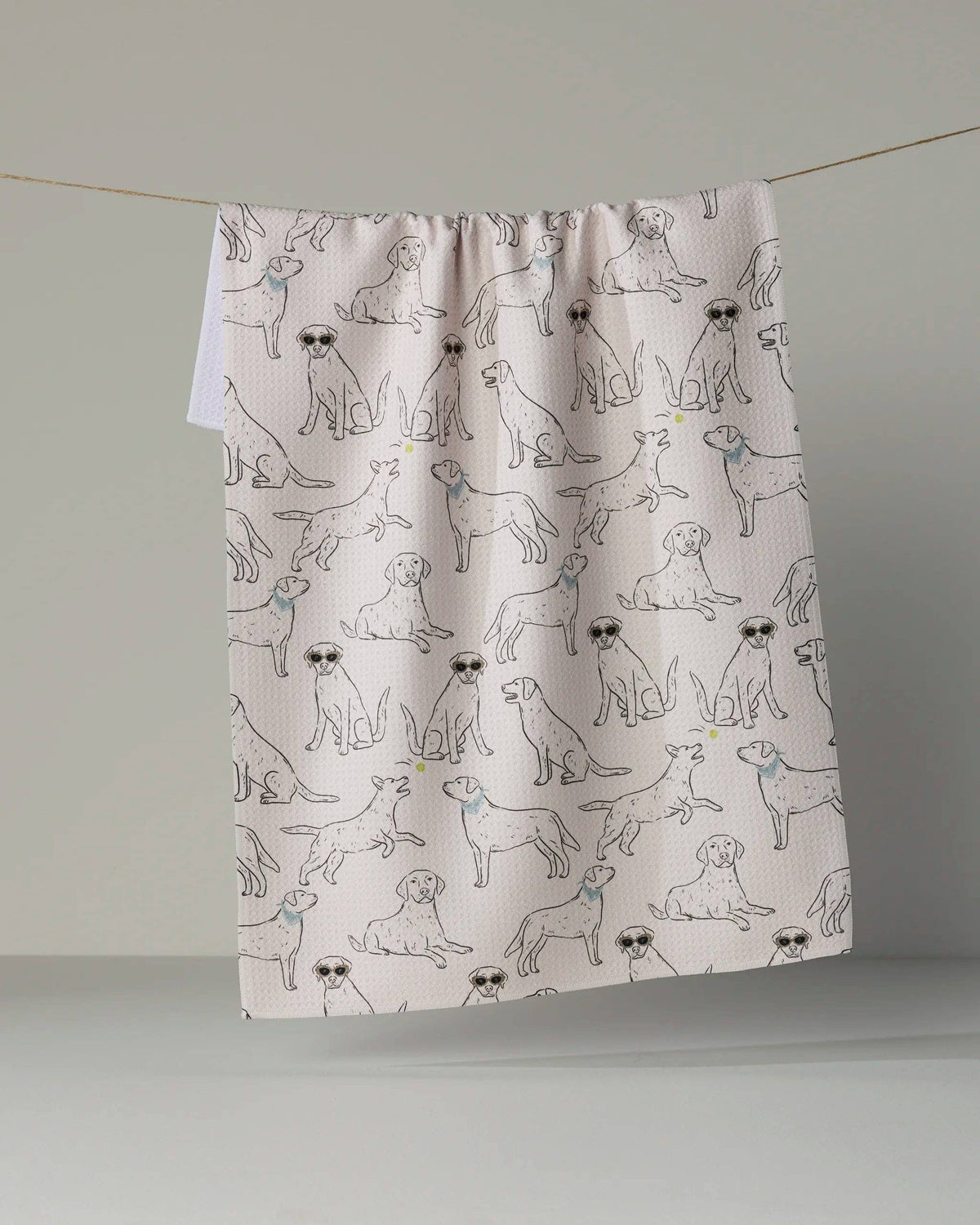 A fabric curtain panel with a repeating pattern of illustrated dogs in black and blue, hanging from a thin string against a plain light gray wall.