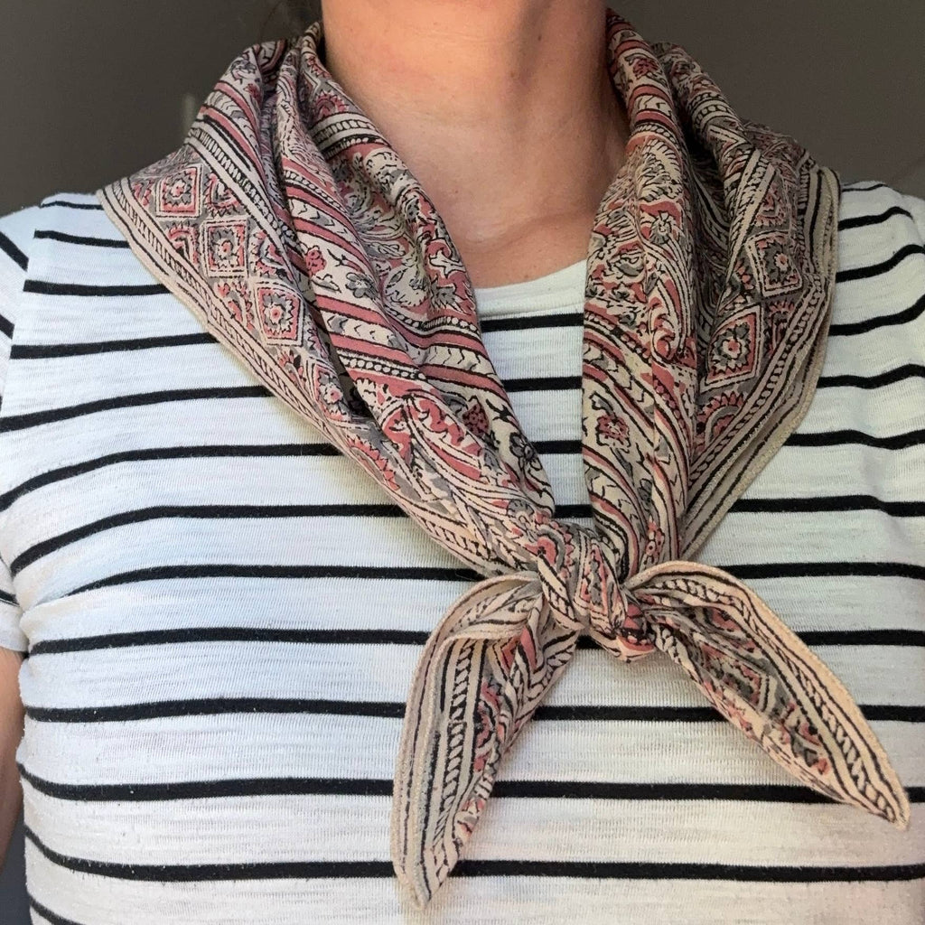 A close-up of a person wearing a patterned scarf tied around the neck over a black and white striped shirt. The scarf features a detailed paisley and geometric design in beige, brown, and muted red.