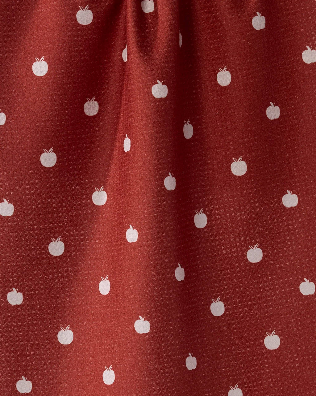 A close-up of a rust red or terracotta fabric with a repeating pattern of small white apples.