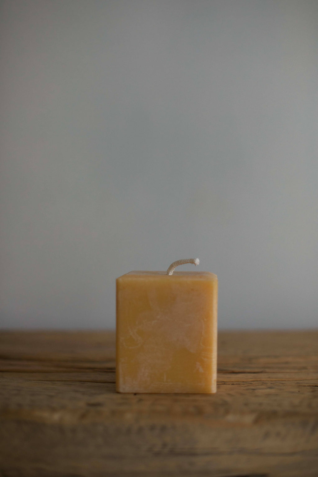 Square beeswax candle on a wooden surface with a gray background
