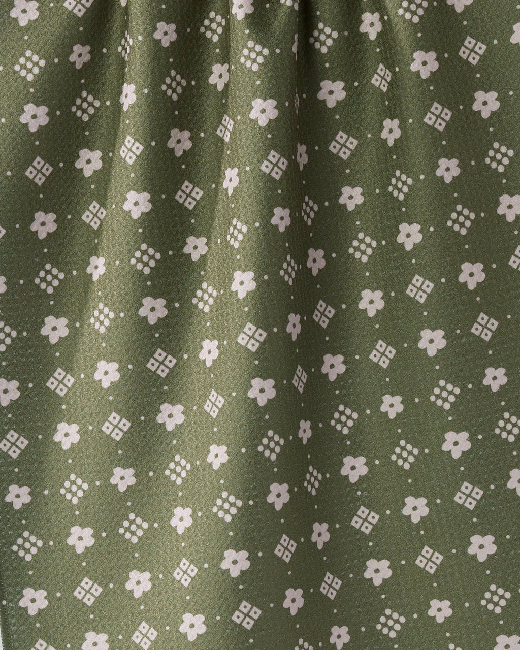 Close-up of olive green fabric with a repeating white floral and geometric pattern.
