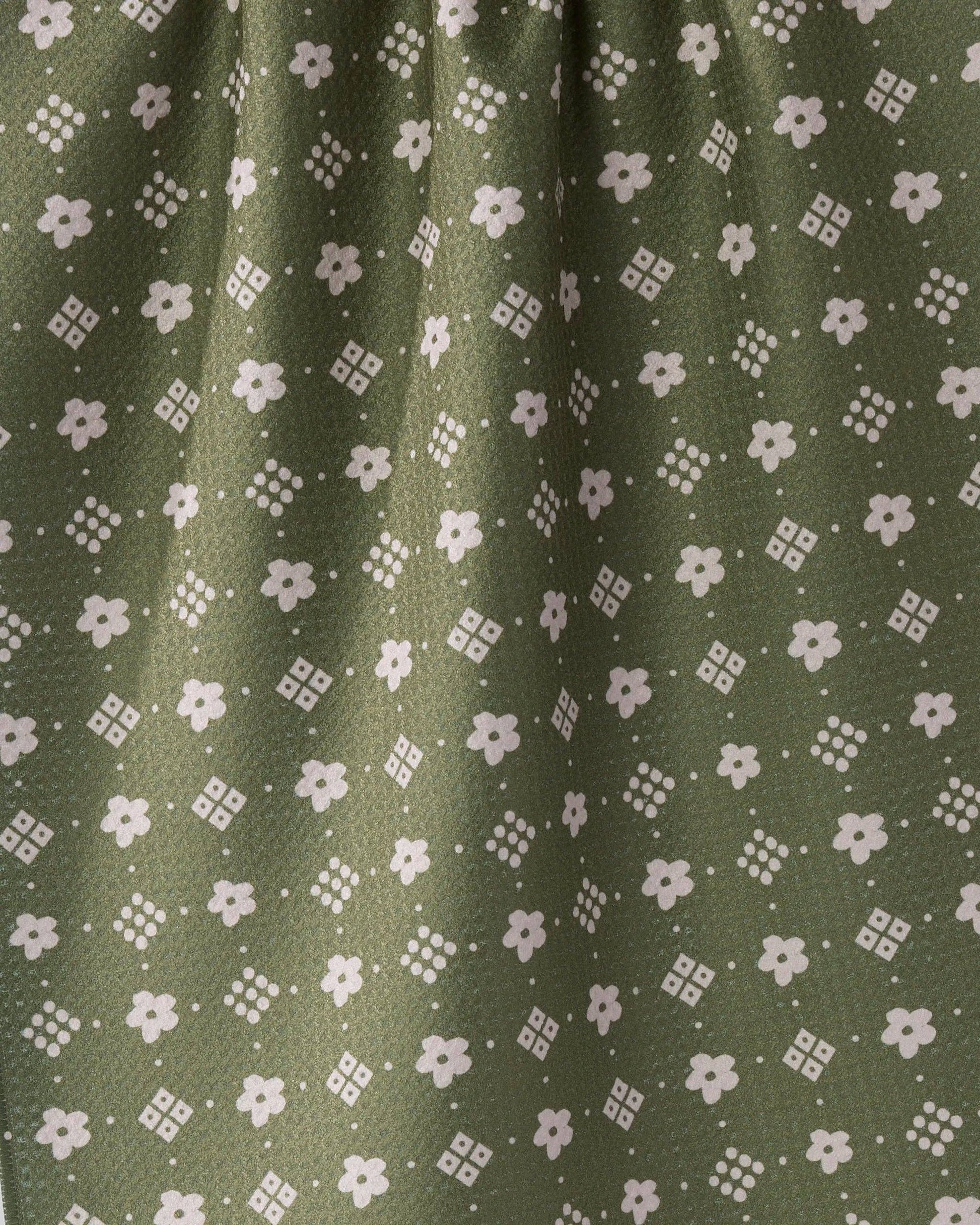 Close-up of olive green fabric with a repeating white floral and geometric pattern.
