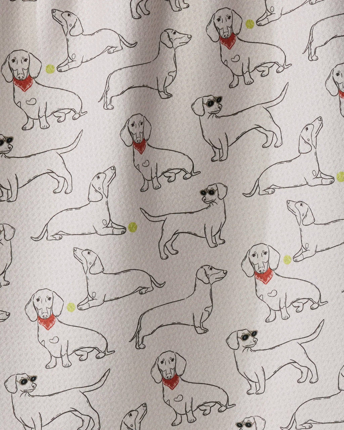A close-up of a fabric or paper surface with an allover print of dachshund illustrations. The dogs are drawn in black outline with small red bandanas and a few have tiny yellow accents.