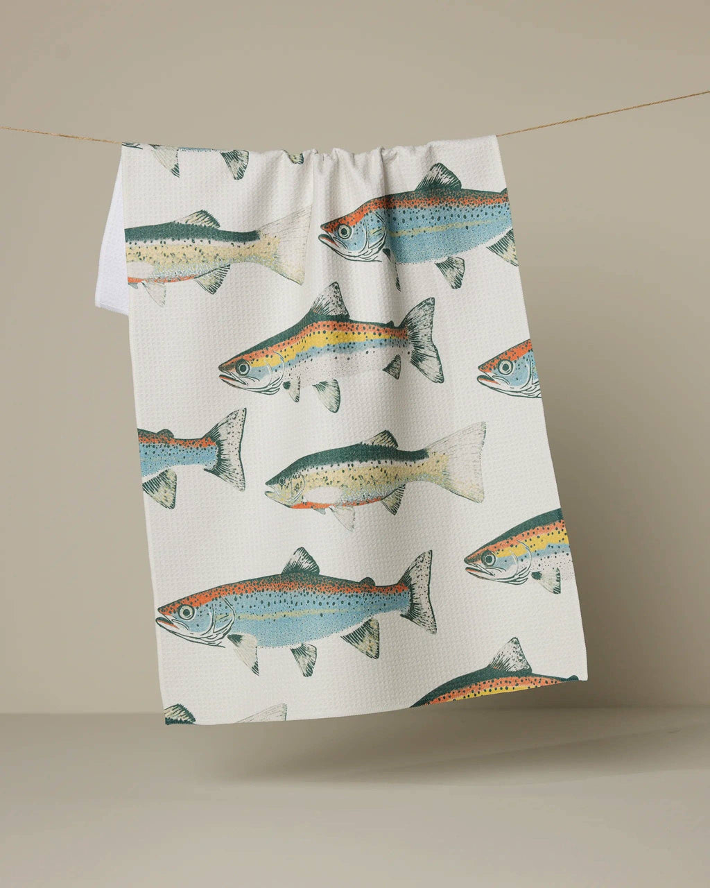 Tea towel with fish pattern hanging on a line against a beige background