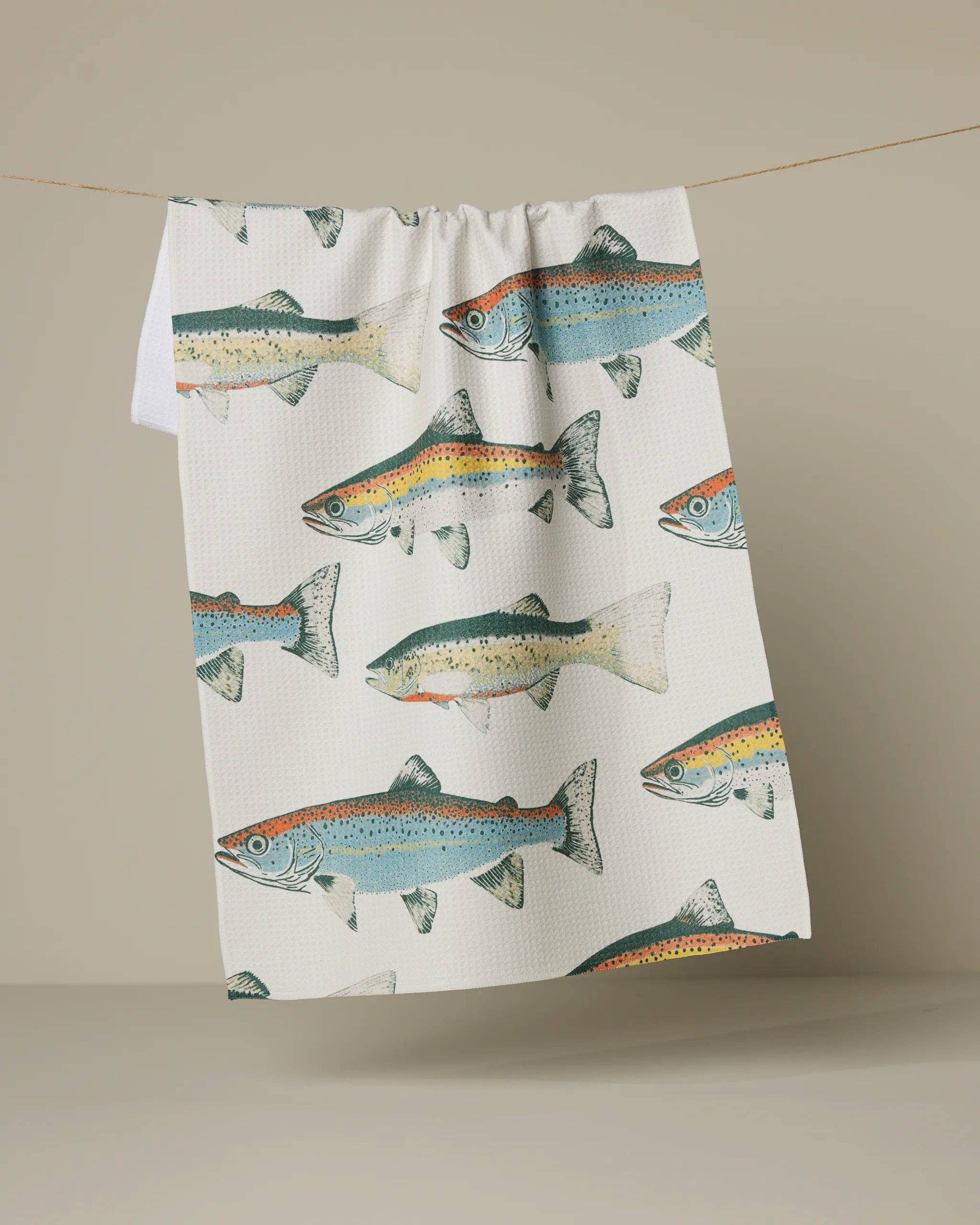 Tea towel with fish pattern hanging on a line against a beige background