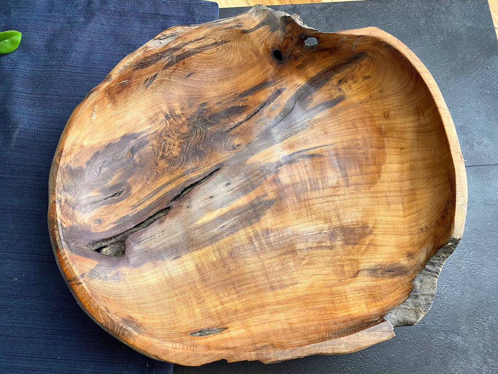 A rustic handcrafted wooden bowl made from a live-edge tree trunk, showcasing natural grain patterns and dark knots, set against a dark textured background.