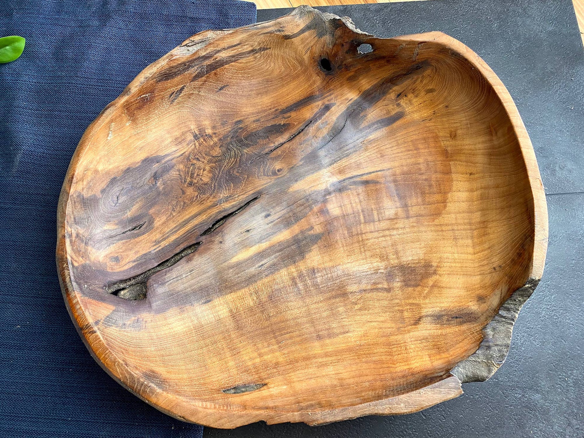 A rustic handcrafted wooden bowl made from a live-edge tree trunk, showcasing natural grain patterns and dark knots, set against a dark textured background.