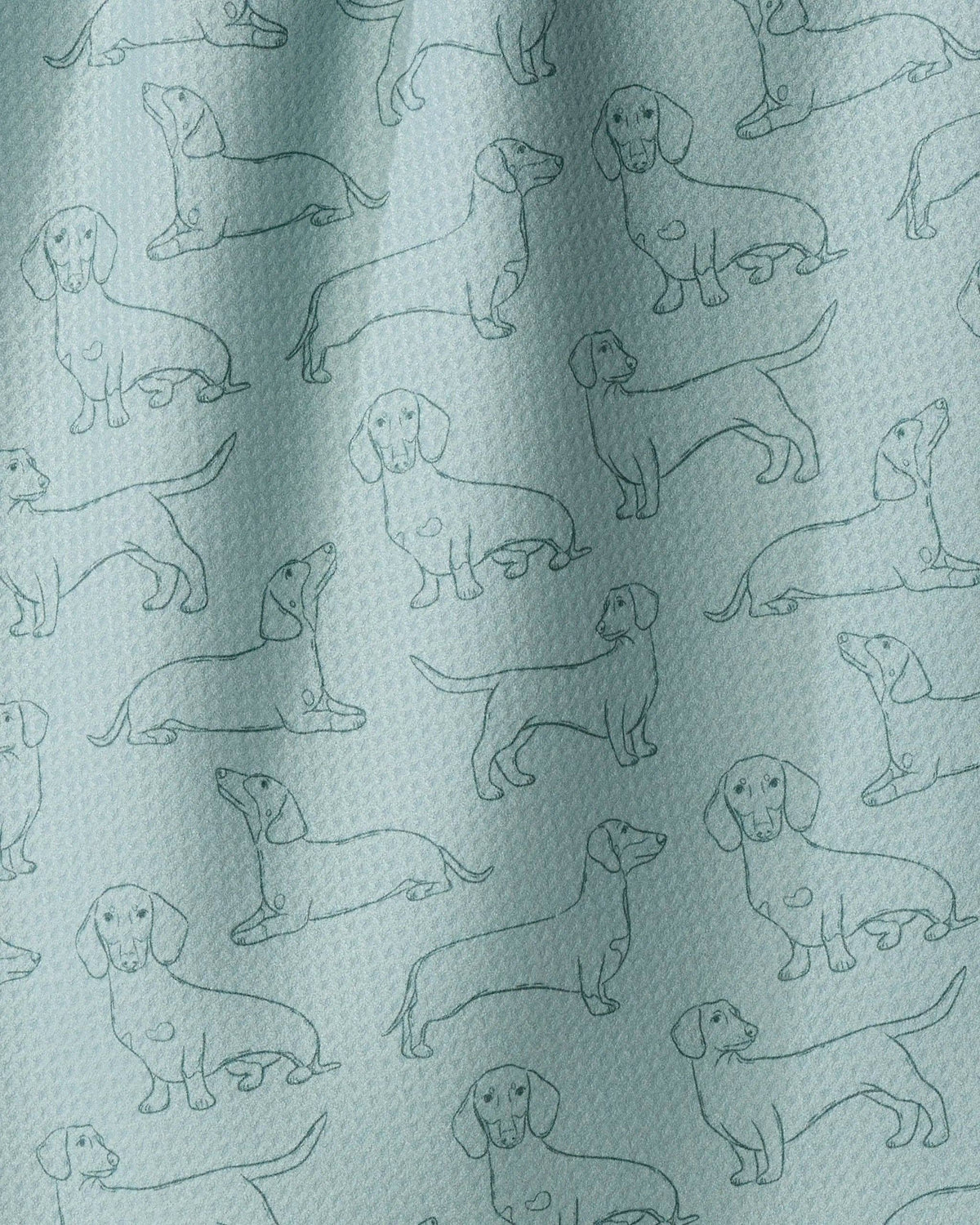 A close-up of a fabric surface with a repeating pattern of dachshund dog illustrations in dark teal on a pale mint-green background.