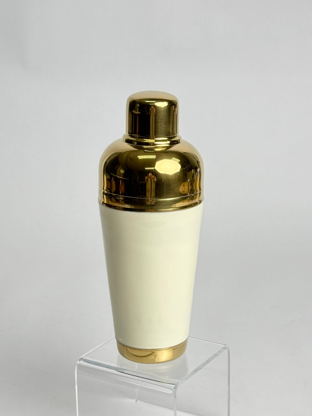 Gold and white cocktail shaker on a clear stand with a light gray background