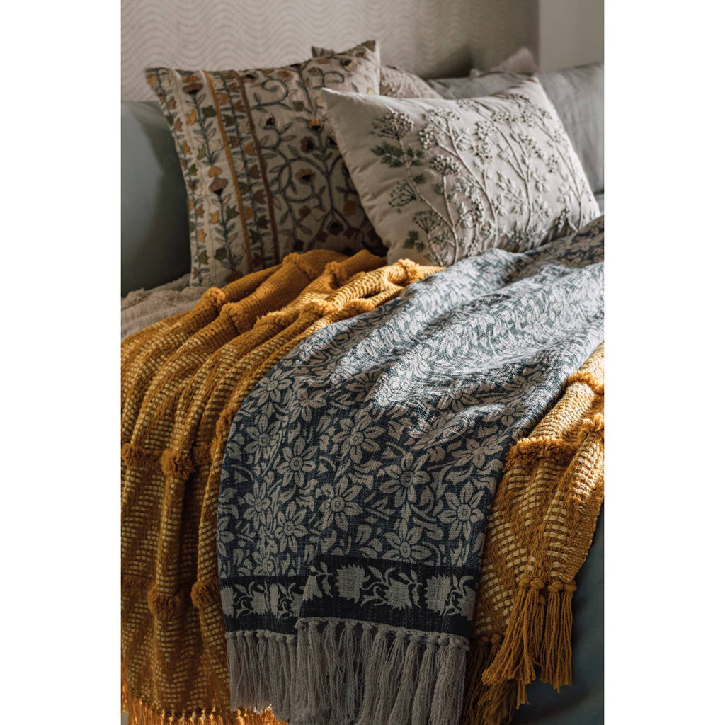 Patterned bedspread with fringes on a bed with decorative pillows.