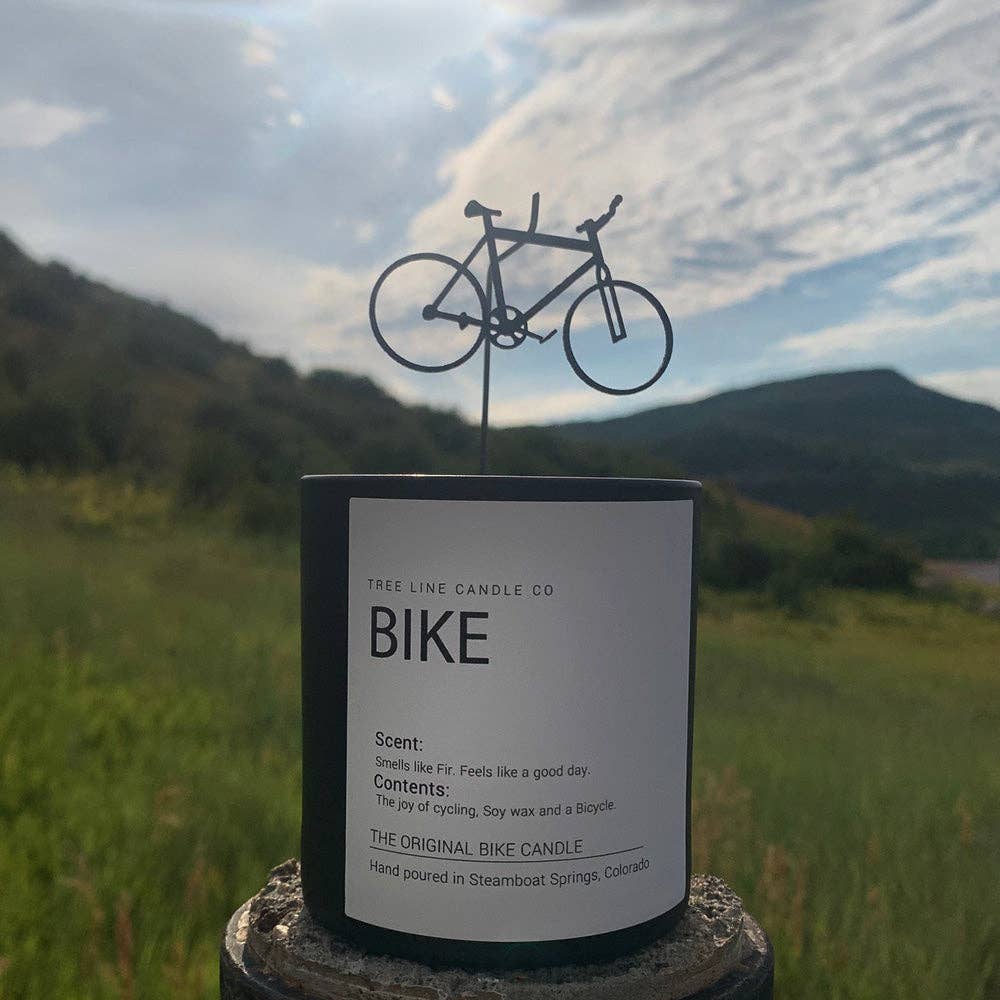 Candle labeled 'Bike' with a bicycle design on top, set against a scenic background.