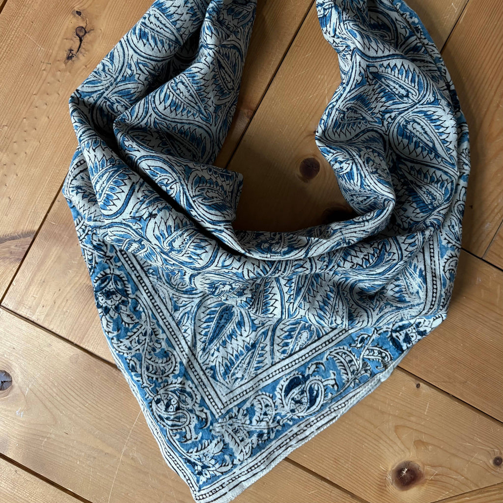 A blue and white paisley bandana scarf laid flat on a light-colored wooden floor.