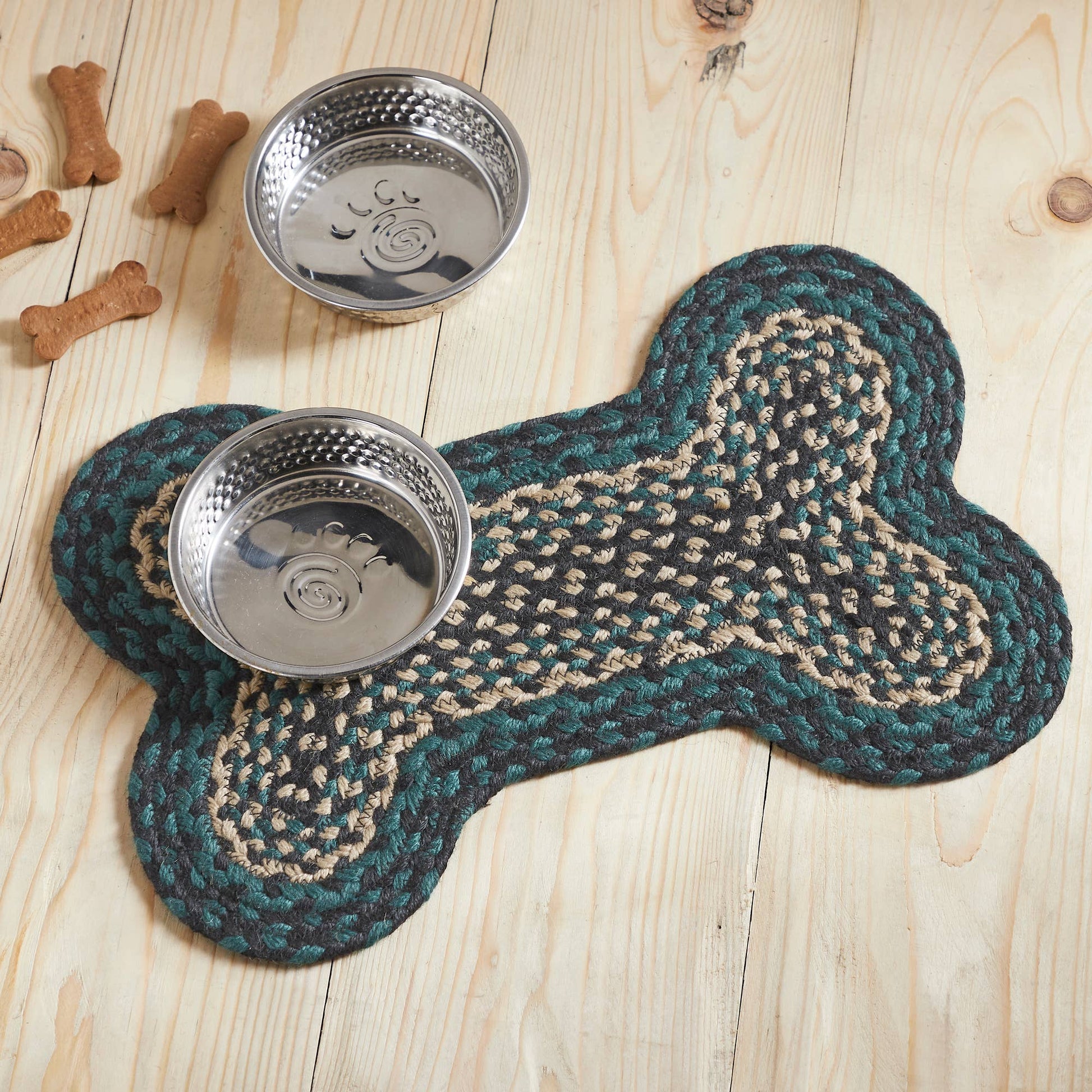 Dog bone-shaped mat with two metal bowls on a wooden surface, surrounded by dog treats.