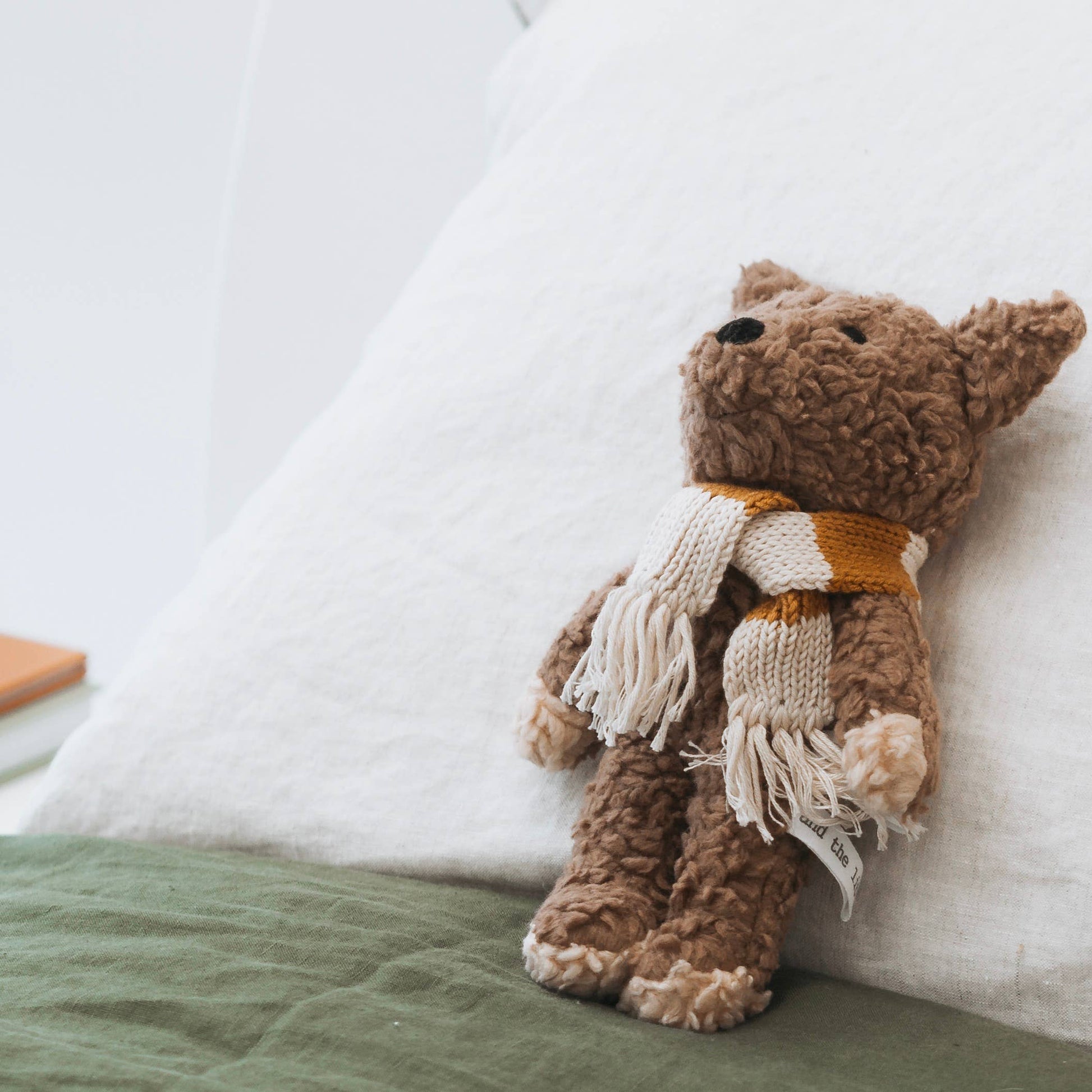 A plush toy resembling a dog with a striped knitted scarf, placed on a bed.