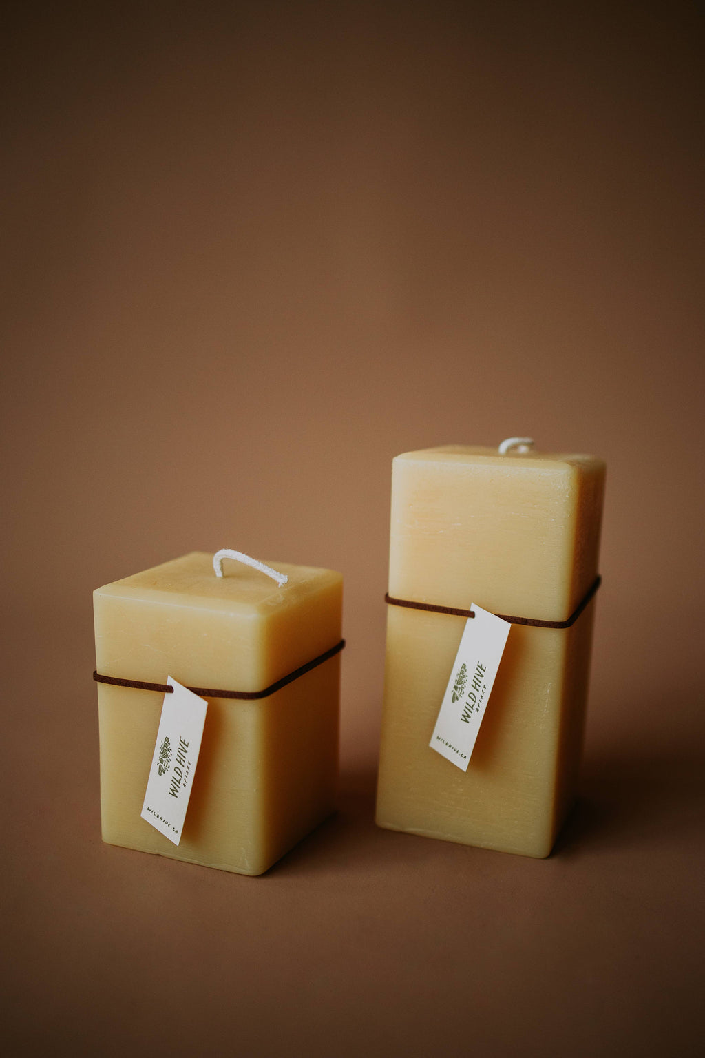 Three square beeswax candles with labels on a brown background