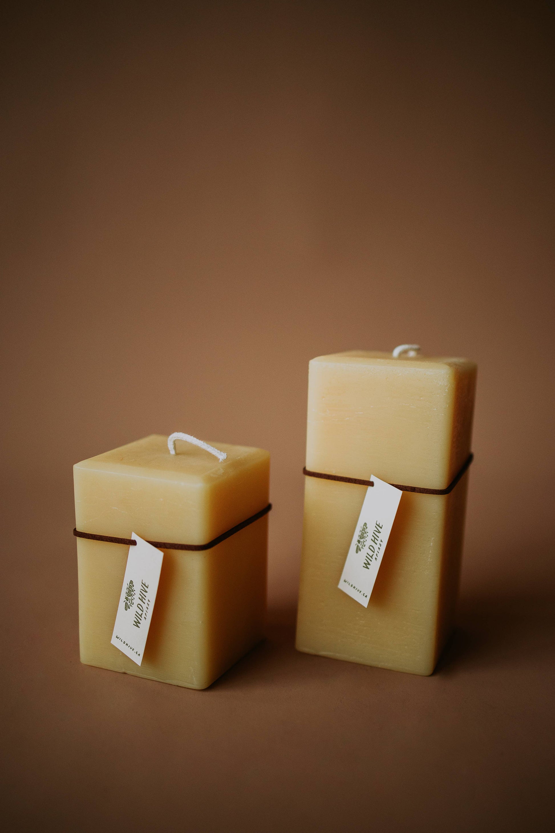 Three square beeswax candles with labels on a brown background