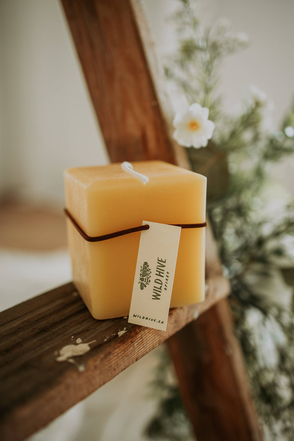 Square beeswax candle with a visible brand tag on a wooden surface.